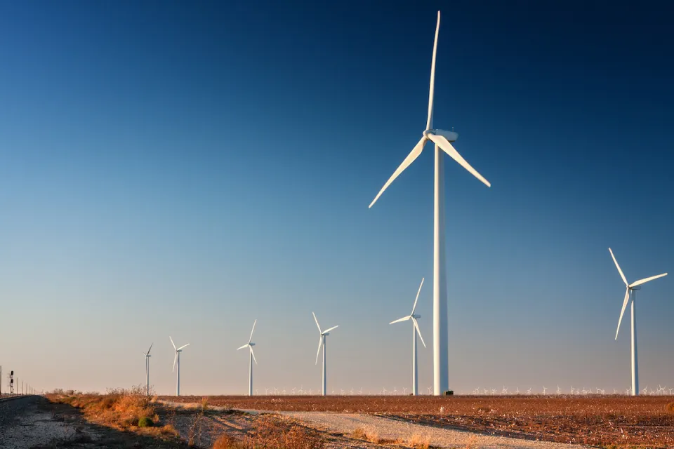 Row of white wind turbines in wide open dirt field in west Texas.